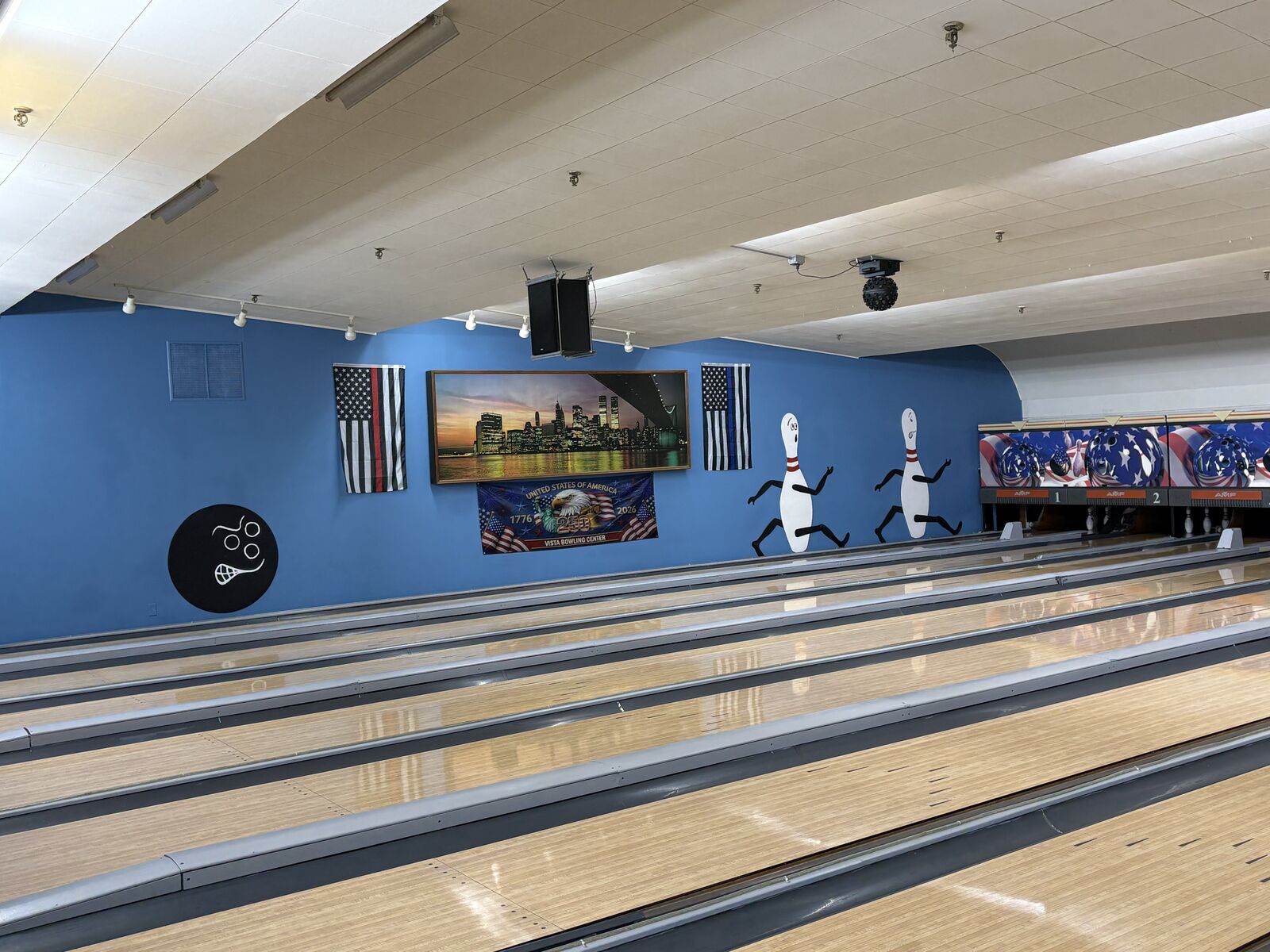 Bowling lanes with flags, a city skyline picture, and cartoon pins on the blue wall