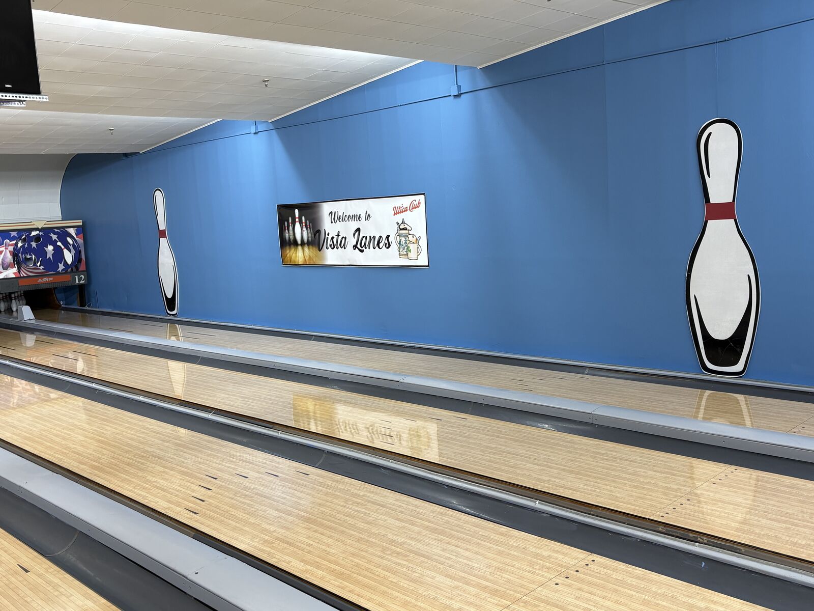 Bowling lanes looking toward a blue wall with a Welcome to Vista Lanes sign and pin graphics